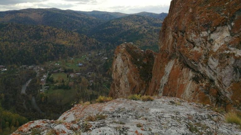 rock mountain overlooking trees and houses near the river
